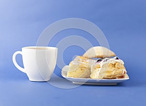 White ceramic cup of hot coffee and sweet pastries on blue background