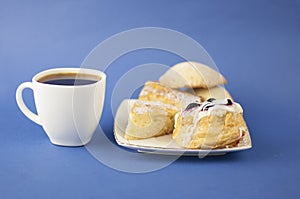 White ceramic cup of hot coffee and sweet pastries on blue background