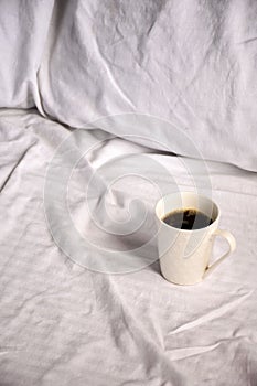White ceramic mug with freshly brewed coffee atop a bed of crisp, white sheets