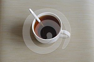 A white ceramic mug full of black tea with a metal spoon