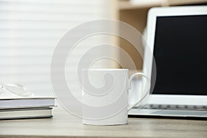 White ceramic mug, notebooks and laptop on wooden table indoors