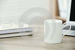 White ceramic mug, notebooks and laptop on wooden table indoors. Space for text