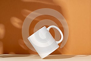 White ceramic mug on peach background with shadows close up