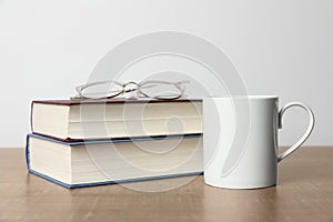 White ceramic mug, stack of books and glasses on wooden table