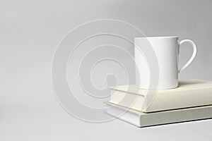 White ceramic mug and stack of books on light background, space for text