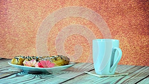 A white ceramic mug with tea and a plate with three eclairs and a red flower stand on a wooden table