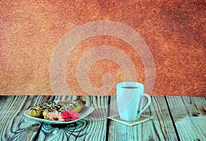 A white ceramic mug with tea and a plate with three eclairs and a red flower stand on a wooden table