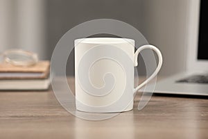 White ceramic mug on wooden table at workplace