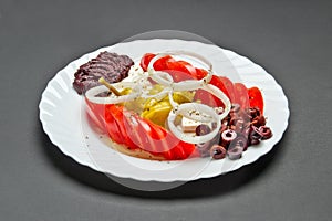 White ceramic plate with marinated olives, tomatoes, pepper, onion, feta cheese, olive oil and spice mix
