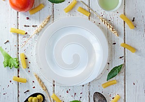 White ceramic plate surrounded by italian tortiglioni pasta, bay leaves and other ingredients.