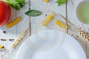 White ceramic plate surrounded by italian tortiglioni pasta, bay leaves and other ingredients.