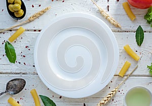 White ceramic plate surrounded by italian tortiglioni pasta, bay leaves and other ingredients.