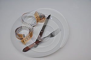 White ceramic plate with yellow measuring tape, fork and knife on white background