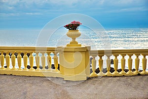 White ceramic pot with red geraniums on the blue sea background in sunny summer day. A terrace overlooking the sea. The best place