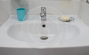 White ceramic sink in bathroom with plastic glass for brush and soap for hand cleaning