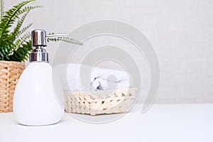 White ceramic soap dispenser, spa towel and green plan on white counter table inside a bright bathroom background with