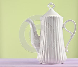 White ceramic teapot on a pastel purple wooden table isolated on