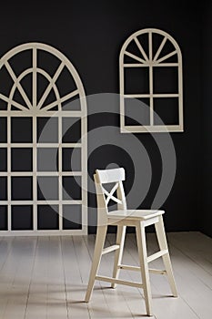 White chair on dark background.The wall is decorated with details in the form of arched doors and arched Windows