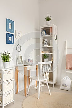 White chair at dressing table next to cabinet with plant in bedroom interior with posters. Real photo