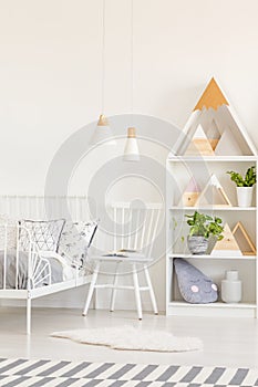 White chair and fur next to kid`s bed in bright bedroom interior