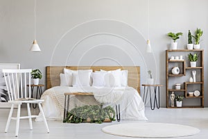 White chair near bed with wooden headboard in bright bedroom int