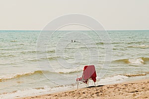 White chair with red cover standing at the summer beach in front of sea and couple in love in the water