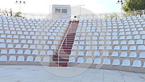 White chairs of an empty amphitheater or stadium under the open sky. A row of seats without spectators