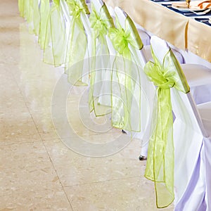 White chairs with green ribbon in wedding