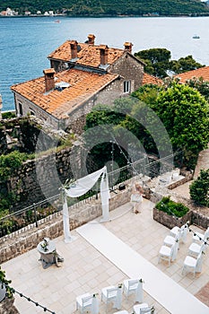 White chairs stand in front of a wedding arch decorated with flowers and fabric on a tiled floor