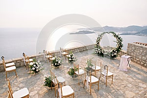 White chairs stand in rows in front of a wedding arch and reception table on an observation deck over the sea