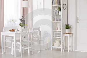 White chairs and table with flowers under lamp in dining room interior with lavender flowers. Real photo