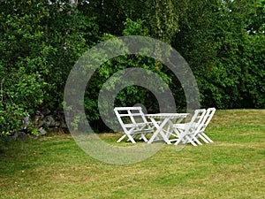 White chairs and table on lawn of garden in landscape format.