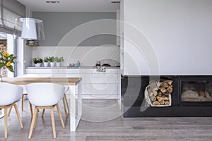 White chairs at wooden table in modern dining room interior with lamp and fireplace. Real photo