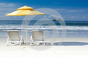 2 white chairs and yellow umbrella on tropical beach