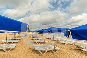 White chaise lounges and blue umbrellas stand on the beach in th