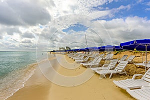 White chaise lounges and blue umbrellas stand on the beach in th