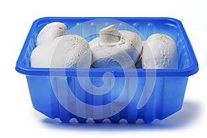 White champignon mushrooms in a blue plastic tray on isolated background. Farmed product for sale in a shop or market. Agriculture