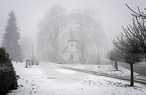 White chapel in fog in winter village and trees