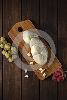 White cheese pigtail with red and green grapes on a wooden cutting board