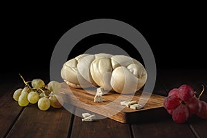 White cheese pigtail with red and green grapes on a wooden cutting board
