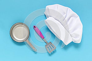 White chef hat on the blue background with kiddish toy utensils.