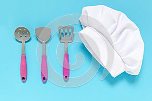 White chef hat with kiddish toy utensils on the blue background . photo