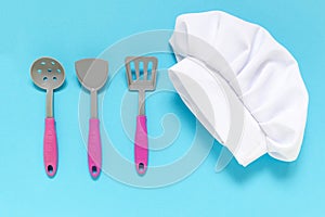 White chef hat with kiddish toy utensils on the blue background .