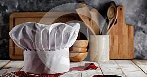 White chef`s hat and wooden table background with kitchen utensils
