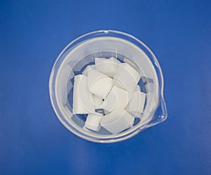 White chemical ingredient in clear beaker on blue table background for science lab experiment.
