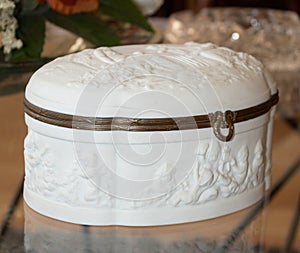 White chest with angels embroided and wooden edges on a glass table