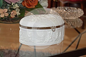 White chest with angels embroided and wooden edges on a glass table