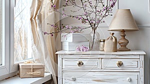 a white chest of drawers adorned with a bottle of pink flowers, a stylish lamp, and gift bags and boxes with delicate