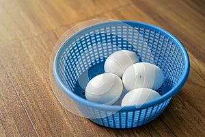 4 white chicken eggs in blue plastic basket on wood floor. 1 of 4 Chicken is ready to break out the egg shell from inside