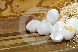 White chicken eggs and broken eggs on wooden board or table.